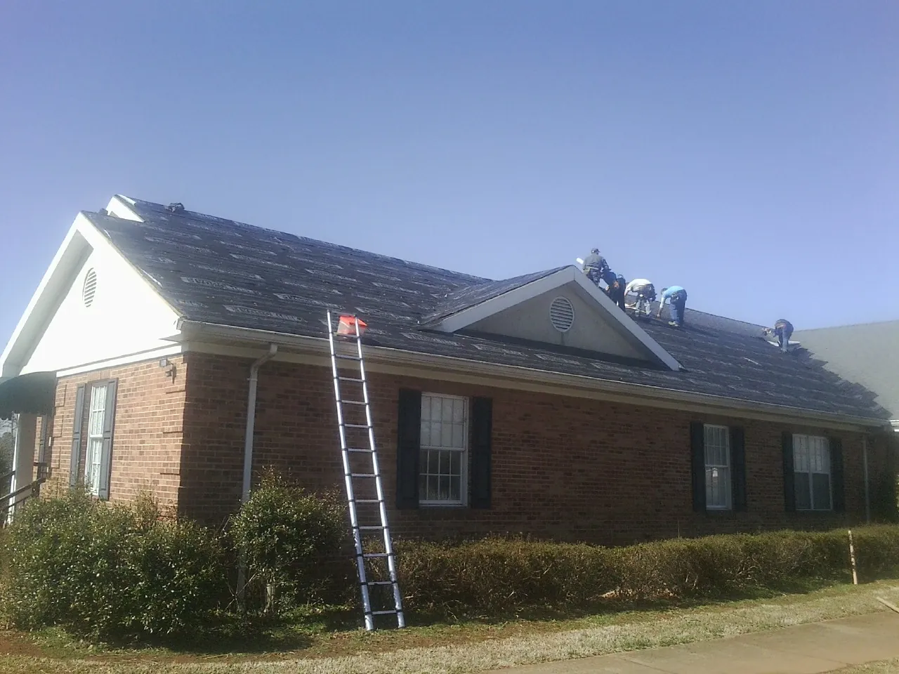 Crew tearing shingles off a brick ranch roof with a ladder set — Emergency Roof Repair work by our crew in Acme