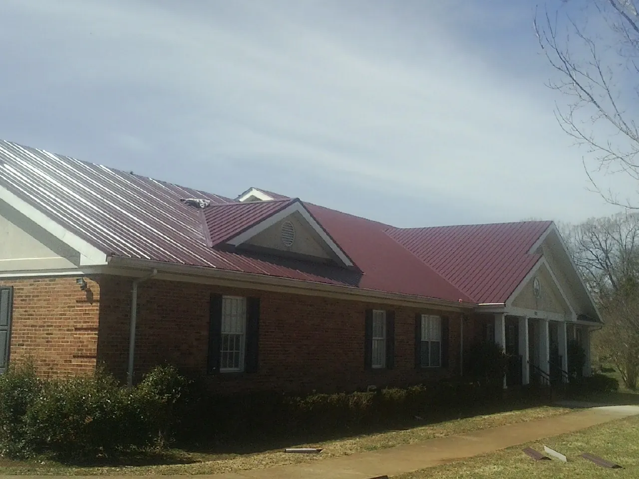 Red metal roof with gabled entries on a long brick building, from a Hail Damage Roof Repair job in Acme