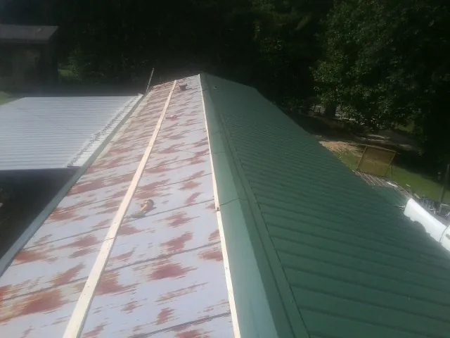 Old rusted panels beside newly installed green metal roofing — Wind Damage Roof Repair by Roofing Brothers in Acme