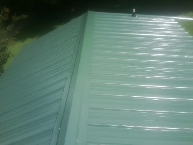 New green metal panels meeting at the ridge of a roof — Flat Roof Repair work by our crew in Acme