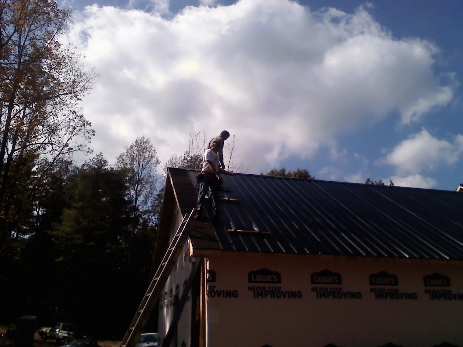 Roofer fastening dark metal panels high against a cloudy sky, from a Roof Inspection job in Acme
