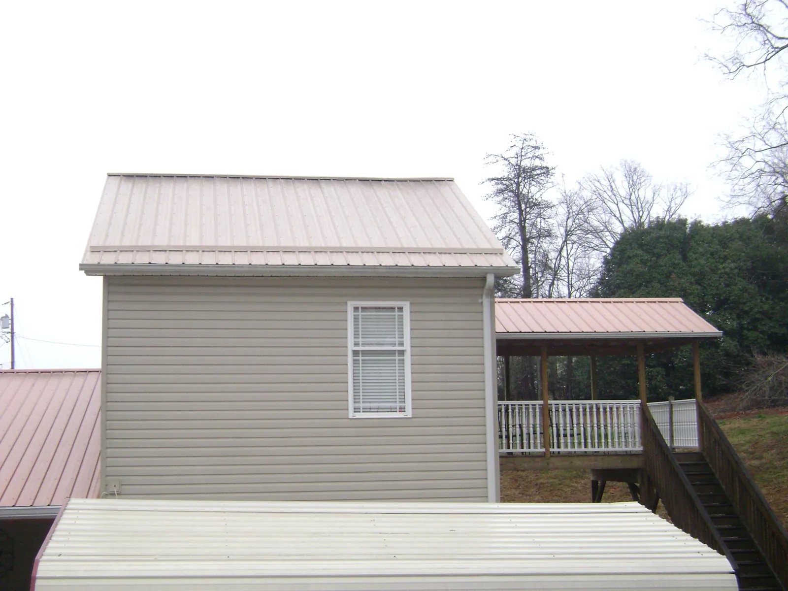 Tan metal roofs on a two story addition and attached porch, from a Roof Replacement job in Acme